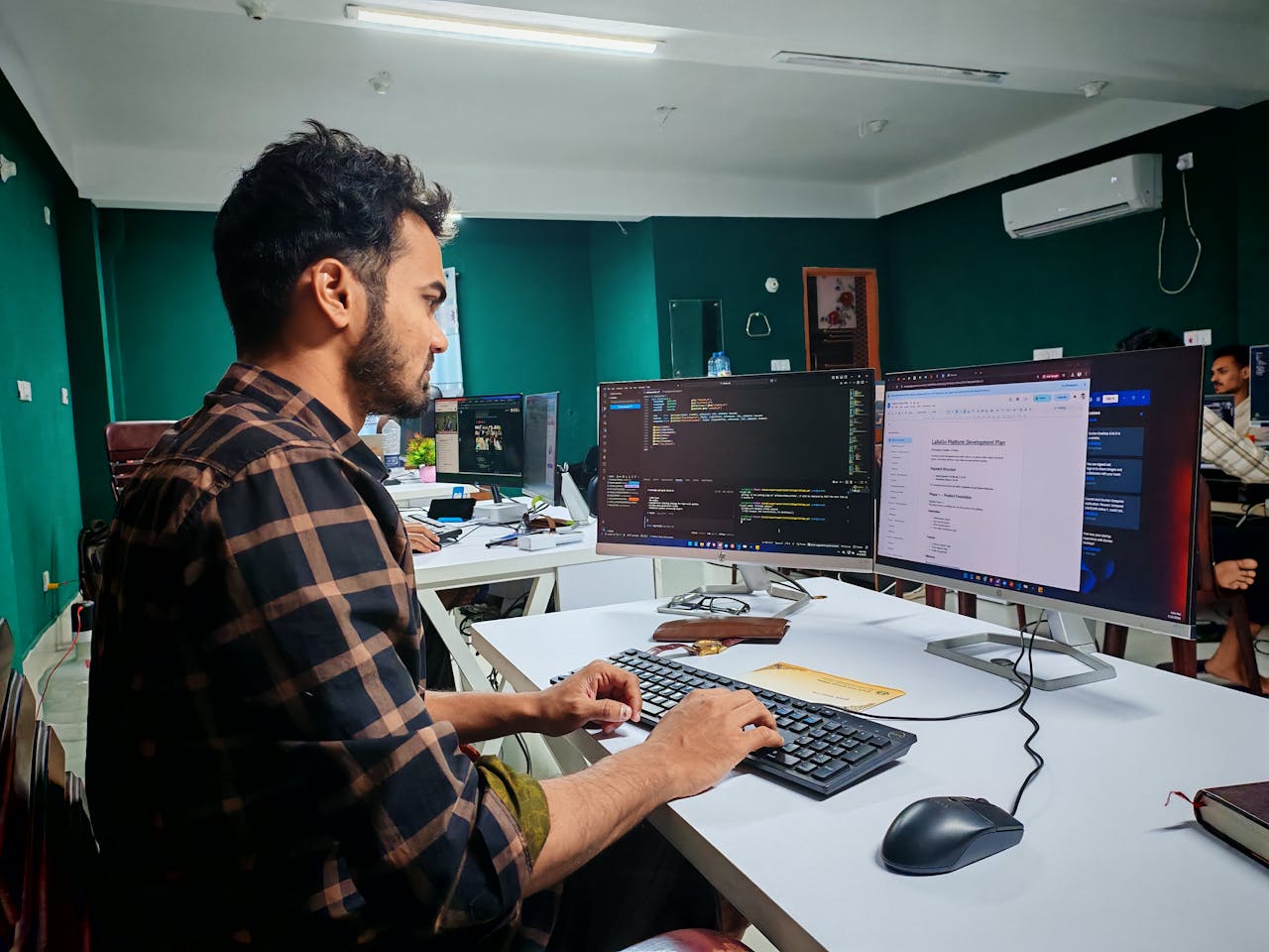 services-04 A software developer working on code at a dual monitor setup in a modern office.